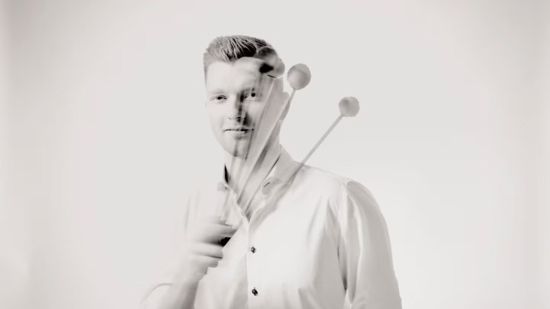 Ein Mann in einem weißen Hemd hält mehrere Schlägel in der Hand, die in Bewegung sind. Das Bild ist in Schwarz-Weiß gehalten., © Marco Borggreve Ein Mann in einem weißen Hemd hält mehrere Schlägel in der Hand, die in Bewegung sind. Das Bild ist in Schwarz-Weiß gehalten., © Marco Borggreve