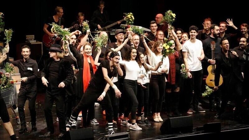 Eine große Gruppe von Menschen auf einer Bühne feiert mit Blumensträußen in den Händen. Einige tragen schwarze Kleidung, andere sind in Weiß gekleidet., © STUTTGARTER NACHRICHTEN Eine große Gruppe von Menschen auf einer Bühne feiert mit Blumensträußen in den Händen. Einige tragen schwarze Kleidung, andere sind in Weiß gekleidet., © STUTTGARTER NACHRICHTEN