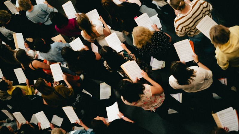 Eine Gruppe von Menschen h&auml;lt Notenbl&auml;tter und probt gemeinsam in einem Chor. Die Aufnahme zeigt sie von oben., &copy; StadtPalais