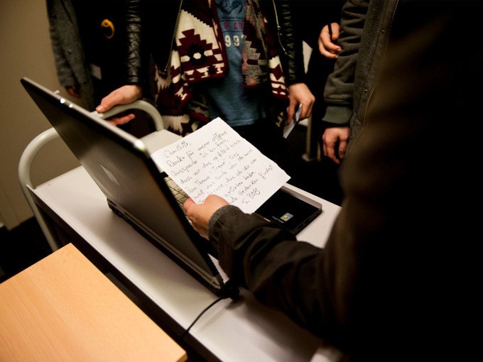 Person holding a handwritten note in front of a laptop, surrounded by several people. The piece of paper contains notes., © Landesmuseum Württemberg Person holding a handwritten note in front of a laptop, surrounded by several people. The piece of paper contains notes., © Landesmuseum Württemberg