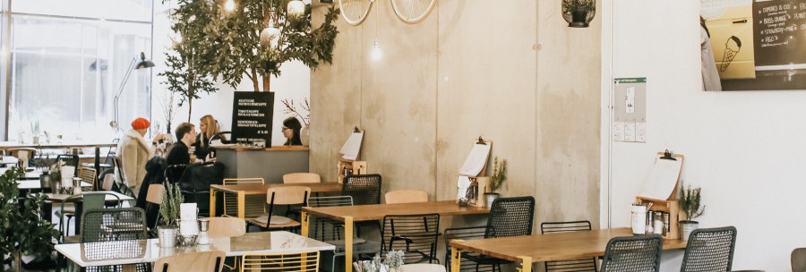 Modern café with a hanging bicycle on the wall, plants and cozy seating areas. People sit and chat at tables., © Claus Stuttgart