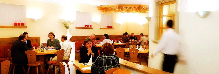 Gem&uuml;tliches Restaurant mit Holzm&ouml;beln, mehreren G&auml;sten an Tischen und einem Kellner in Bewegung. Warme Beleuchtung und dekorative Elemente an den W&auml;nden., &copy; SMG