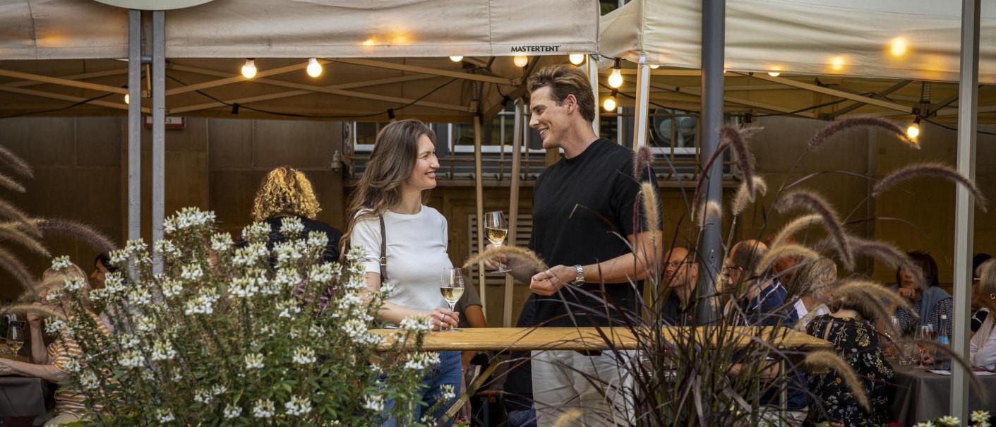 Zwei Personen stehen lächelnd mit Weingläsern in der Hand auf dem Stuttgarter Weindorf. Im Hintergrund sind Zelte und weitere Gäste zu sehen., © Stuttgart-Marketing GmbH, Sarah Schmid Zwei Personen stehen lächelnd mit Weingläsern in der Hand auf dem Stuttgarter Weindorf. Im Hintergrund sind Zelte und weitere Gäste zu sehen., © Stuttgart-Marketing GmbH, Sarah Schmid
