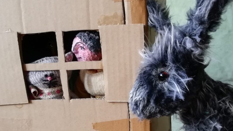 Ein Stoffesel blickt durch ein Pappfenster, hinter dem zwei gestrickte Figuren zu sehen sind. Die Szene wirkt humorvoll und kreativ gestaltet., © FITZ Das Theater animierter Formen Ein Stoffesel blickt durch ein Pappfenster, hinter dem zwei gestrickte Figuren zu sehen sind. Die Szene wirkt humorvoll und kreativ gestaltet., © FITZ Das Theater animierter Formen