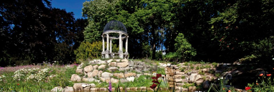 Ein blühender Garten mit bunten Blumen, einem kleinen Teich und einem Pavillon im Hintergrund, umgeben von Bäumen., © Staatsministerium Baden-Württemberg