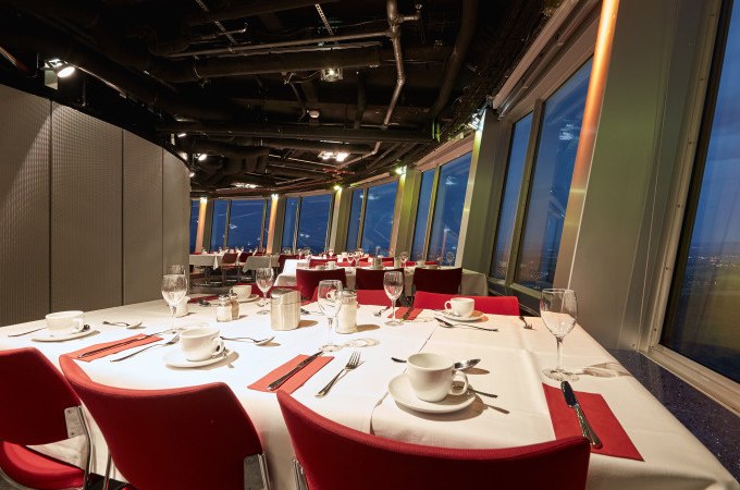 Elegantes Café mit gedeckten Tischen, rotem Dekor und Panoramafenstern, die einen nächtlichen Stadtblick bieten., © SWR Media Services GmbH / SWR Fernsehturm Stuttgart