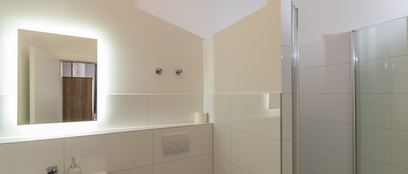 Modernes Badezimmer mit beleuchtetem Spiegel, Waschbecken, Toilette und Dusche. Helle Fliesen und minimalistisches Design., © TOMAS Modernes Badezimmer mit beleuchtetem Spiegel, Waschbecken, Toilette und Dusche. Helle Fliesen und minimalistisches Design., © TOMAS