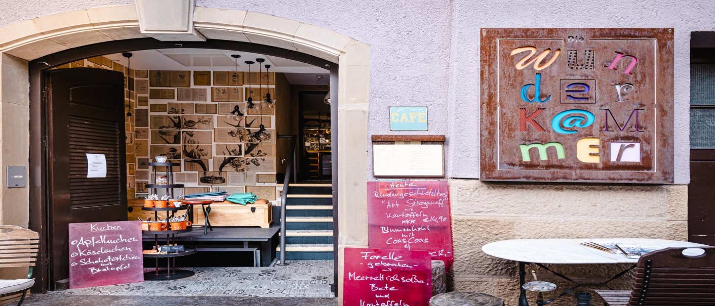 Eingang zur Wunderkammer mit dekorativen Wänden, buntem Schild und Speisekarten. Einladende Atmosphäre mit Café-Charme., © by Canto