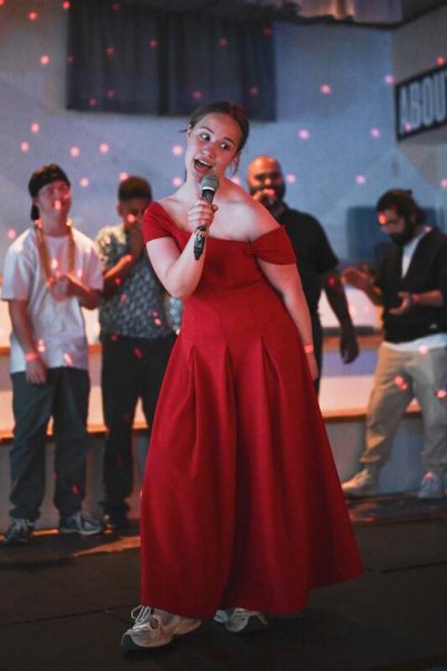 Eine Frau in einem roten Kleid singt auf einer B&uuml;hne. Im Hintergrund stehen mehrere Personen. Die Atmosph&auml;re ist festlich mit bunten Lichtern., &copy; Rosenau Kultur e.V.