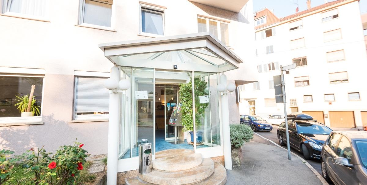 Hoteleingang mit Glasüberdachung und runden Stufen, umgeben von Autos und Pflanzen. Gebäude mit mehreren Fenstern im Hintergrund., © ARNOTEL GmbH Hoteleingang mit Glasüberdachung und runden Stufen, umgeben von Autos und Pflanzen. Gebäude mit mehreren Fenstern im Hintergrund., © ARNOTEL GmbH