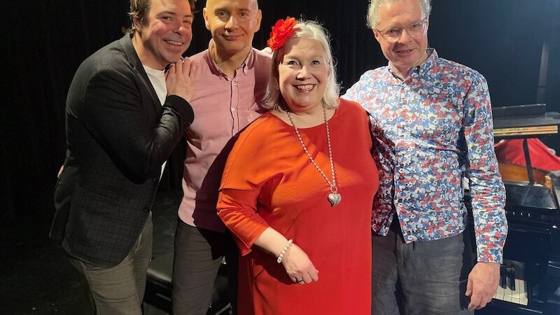 Vier Personen stehen lächelnd vor einem Klavier auf einer Bühne. Sie tragen bunte Kleidung und wirken fröhlich., © Theaterhaus Stuttgart e.V.