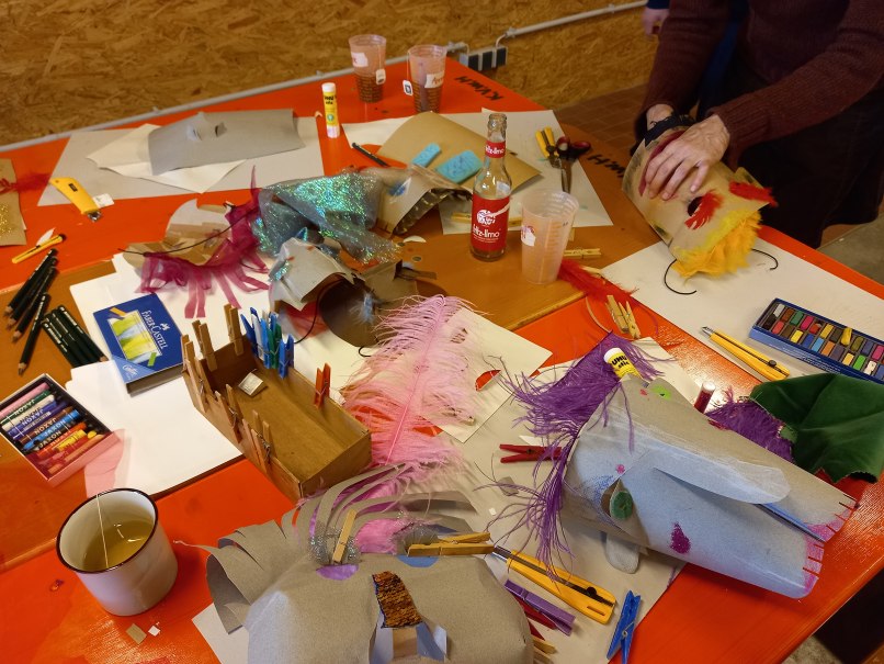 Ein Tisch mit Bastelmaterialien, Masken und Getränken in einem kreativen Workshop. Verschiedene Farben und Texturen sind zu sehen., © KVWH