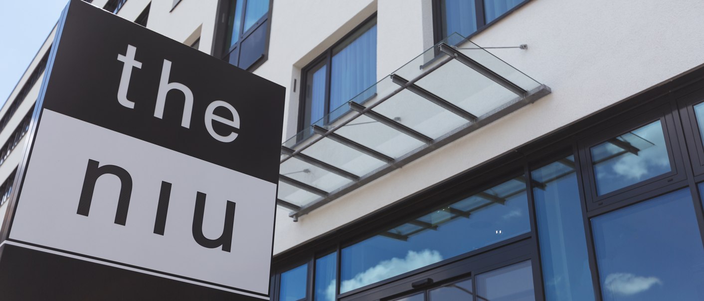 A modern building facade with a glass canopy and the "the niu" sign in the foreground., © the niu Form - Novum Hospitality A modern building facade with a glass canopy and the "the niu" sign in the foreground., © the niu Form - Novum Hospitality