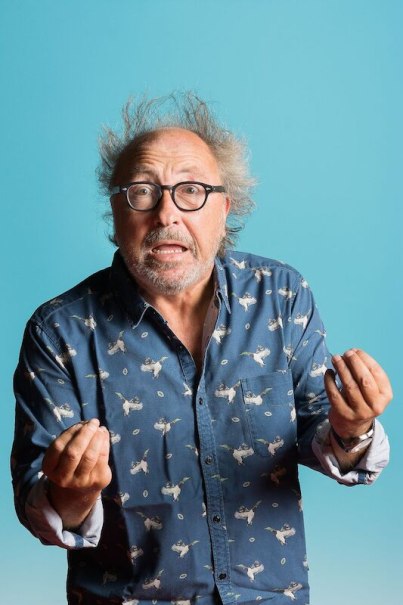 A man with disheveled hair and glasses gesticulates animatedly against a blue background., © Theaterhaus Stuttgart e.V. A man with disheveled hair and glasses gesticulates animatedly against a blue background., © Theaterhaus Stuttgart e.V.