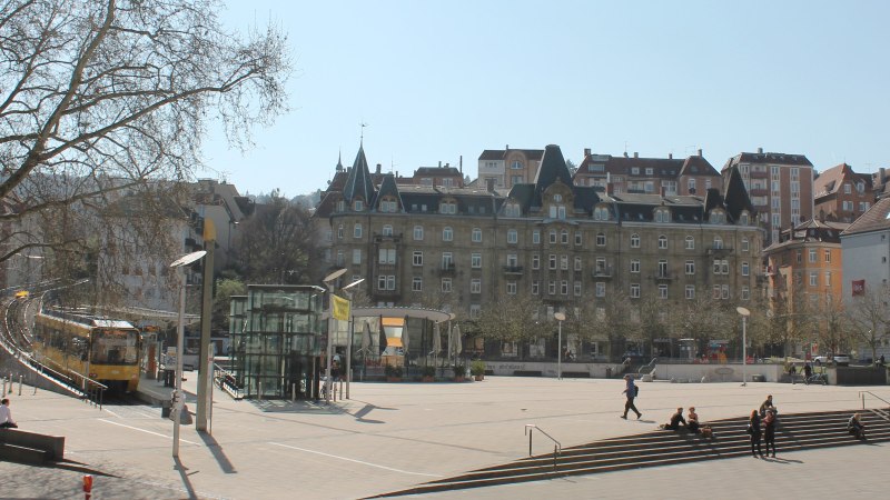 Marienplatz in Stuttgart with streetcar, modern and historic buildings. People sitting on steps, trees without leaves, sunny day., © Stuttgart-Marketing GmbH Marienplatz in Stuttgart with streetcar, modern and historic buildings. People sitting on steps, trees without leaves, sunny day., © Stuttgart-Marketing GmbH