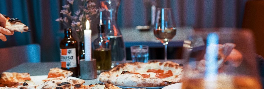 A table in a restaurant with several pizzas, drinks and a burning candle. Glasses and a bottle can be seen in the background., &copy; Italo Disco, Stuttgart