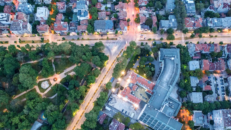 An aerial view of a city at dusk, with illuminated streets, buildings, and green parks. The streets form a grid pattern., © Fraunhofer-Allianz Energie An aerial view of a city at dusk, with illuminated streets, buildings, and green parks. The streets form a grid pattern., © Fraunhofer-Allianz Energie