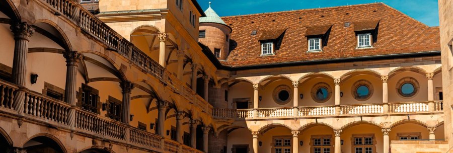 Historischer Innenhof eines Schlosses mit Arkaden, Rundfenstern und einem Turm unter blauem Himmel., © Stuttgart-Marketing GmbH, Sarah Schmid