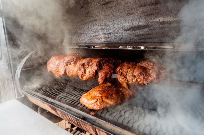 Mehrere Fleischstücke werden in einem Smoker gegrillt, umgeben von dichtem Rauch. Perfekt für ein Winter-BBQ., © Cool-Tours StattReisen Mehrere Fleischstücke werden in einem Smoker gegrillt, umgeben von dichtem Rauch. Perfekt für ein Winter-BBQ., © Cool-Tours StattReisen