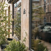 Zwei Personen gehen an einem Geschäft mit der Aufschrift 'Dr. Bohne' vorbei. Die Straße ist von Autos gesäumt, und Pflanzen stehen vor dem Schaufenster., © SMG, Sarah Schmid Zwei Personen gehen an einem Geschäft mit der Aufschrift 'Dr. Bohne' vorbei. Die Straße ist von Autos gesäumt, und Pflanzen stehen vor dem Schaufenster., © SMG, Sarah Schmid