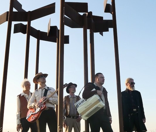 Fünf Männer mit Instrumenten stehen unter einer großen Metallskulptur auf einer Wiese bei Sonnenuntergang., © Rosenau Kultur e.V. Fünf Männer mit Instrumenten stehen unter einer großen Metallskulptur auf einer Wiese bei Sonnenuntergang., © Rosenau Kultur e.V.