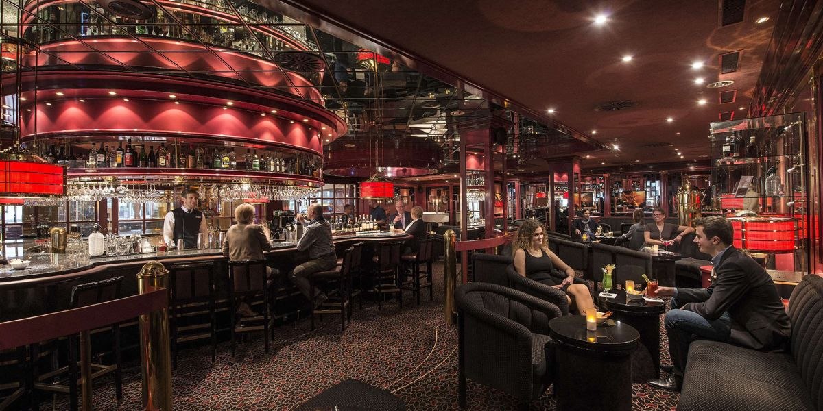 Elegante Bar mit rotem Dekor, Menschen sitzen an Tischen und der Theke, gedämpfte Beleuchtung., © Maritim Hotelgesellschaft mbH Elegante Bar mit rotem Dekor, Menschen sitzen an Tischen und der Theke, gedämpfte Beleuchtung., © Maritim Hotelgesellschaft mbH