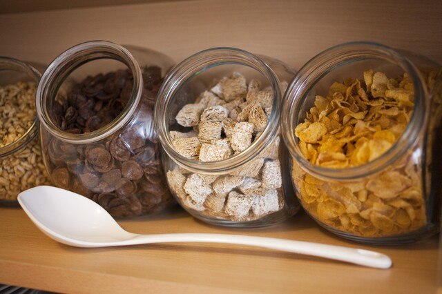 Vier Gläser mit verschiedenen Frühstücksflocken: Schokoladenflakes, Weizenbissen und Cornflakes. Ein weißer Löffel liegt davor., © AKZENT Hotel Torgauer Hof