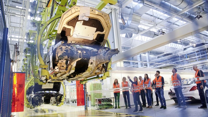 Besucher in orangefarbenen Westen beobachten die Fahrzeugmontage in einer Mercedes-Benz Produktionshalle in Sindelfingen., © Mercedes-Benz AG Besucher in orangefarbenen Westen beobachten die Fahrzeugmontage in einer Mercedes-Benz Produktionshalle in Sindelfingen., © Mercedes-Benz AG