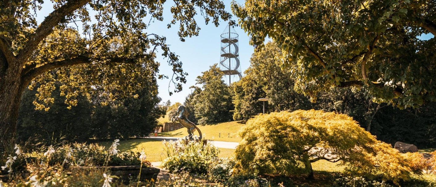 Ein grüner Park mit Bäumen, einer Pferdeskulptur und einem spiralförmigen Aussichtsturm im Hintergrund., © Stuttgart-Marketing GmbH, Sarah Schmid