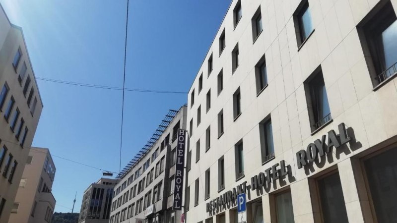 Ein modernes Geb&auml;ude mit dem Schriftzug 'Hotel Royal' unter blauem Himmel. Die Stra&szlig;e ist von weiteren Geb&auml;uden ges&auml;umt., &copy; Hotel Royal