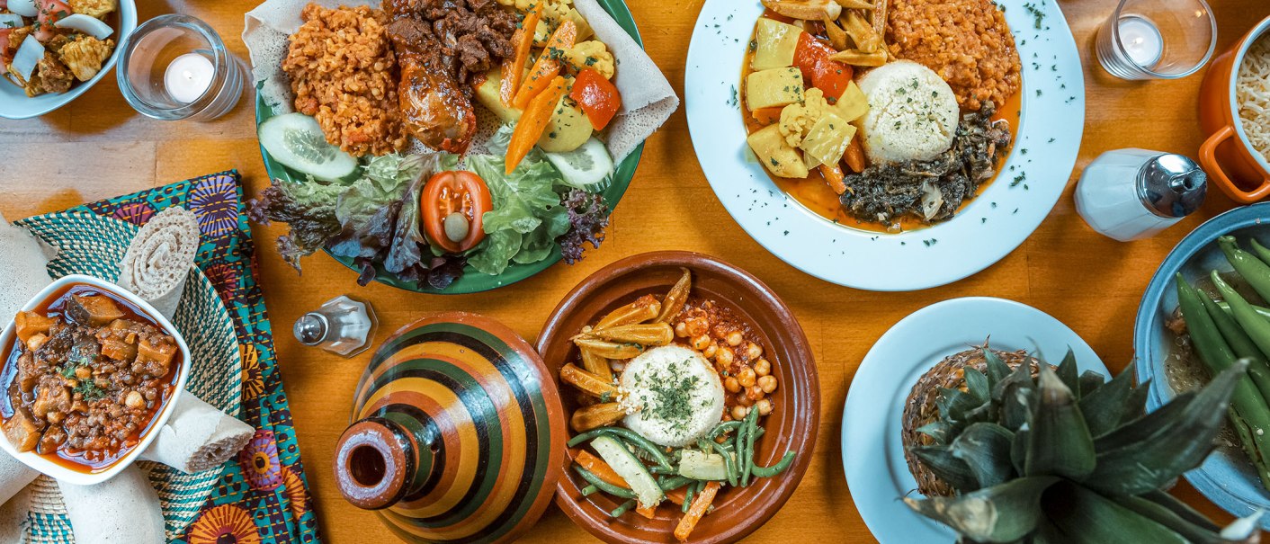 Ein Tisch mit eritreischen Gerichten, darunter Injera, Gemüse und Eintöpfe. Bunte Teller und Schalen mit verschiedenen Speisen., © Dennis Winter Photography