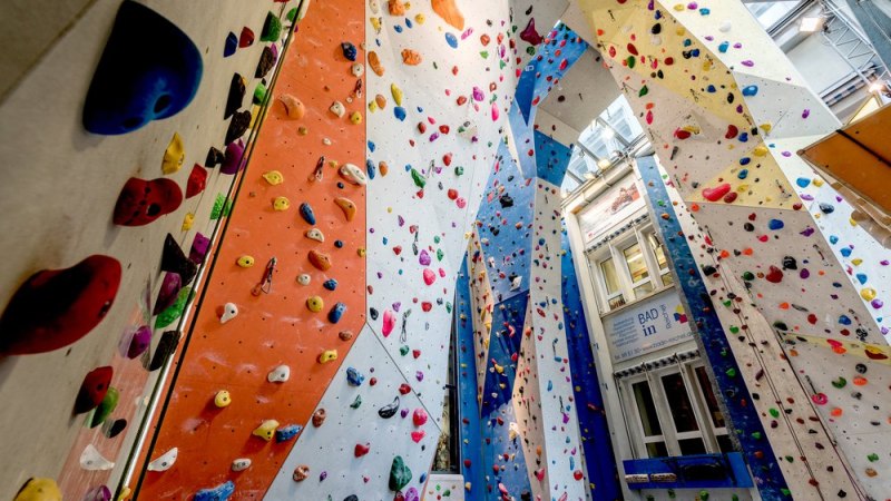 Bunte Klettergriffe an hohen Wänden in der Kletterhalle Cityrock. Die Wände sind in verschiedenen Farben gestaltet und bieten vielfältige Routen., © Kletterhalle Cityrock
