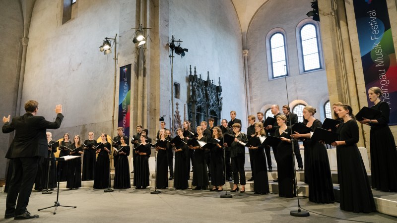 Der Kammerchor der Hochschule für Musik Frankfurt tritt in einer Kirche auf. Der Dirigent leitet den Chor, der in schwarzen Outfits singt., © Kammerchor der Hochschule für Musik Frankfurt Der Kammerchor der Hochschule für Musik Frankfurt tritt in einer Kirche auf. Der Dirigent leitet den Chor, der in schwarzen Outfits singt., © Kammerchor der Hochschule für Musik Frankfurt