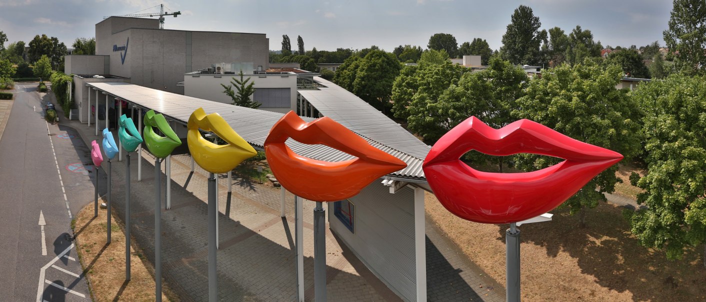 Colorful lip sculptures in various colors in front of the FILharmonie in Filderstadt, surrounded by trees and a cloudy sky., © © Stuttgart-Marketing GmbH Colorful lip sculptures in various colors in front of the FILharmonie in Filderstadt, surrounded by trees and a cloudy sky., © © Stuttgart-Marketing GmbH