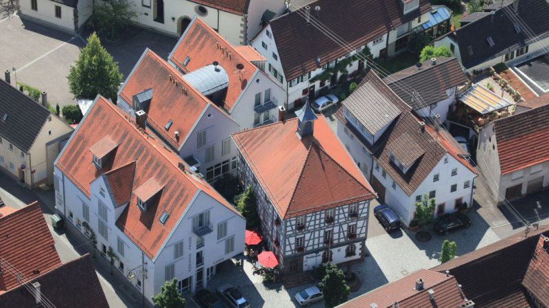 Luftaufnahme eines Dorfes mit Fachwerkhäusern und roten Dächern. Im Zentrum ein Gebäude mit rotem Dach und Sonnenschirmen., © Hotel Gasthof Lamm Luftaufnahme eines Dorfes mit Fachwerkhäusern und roten Dächern. Im Zentrum ein Gebäude mit rotem Dach und Sonnenschirmen., © Hotel Gasthof Lamm