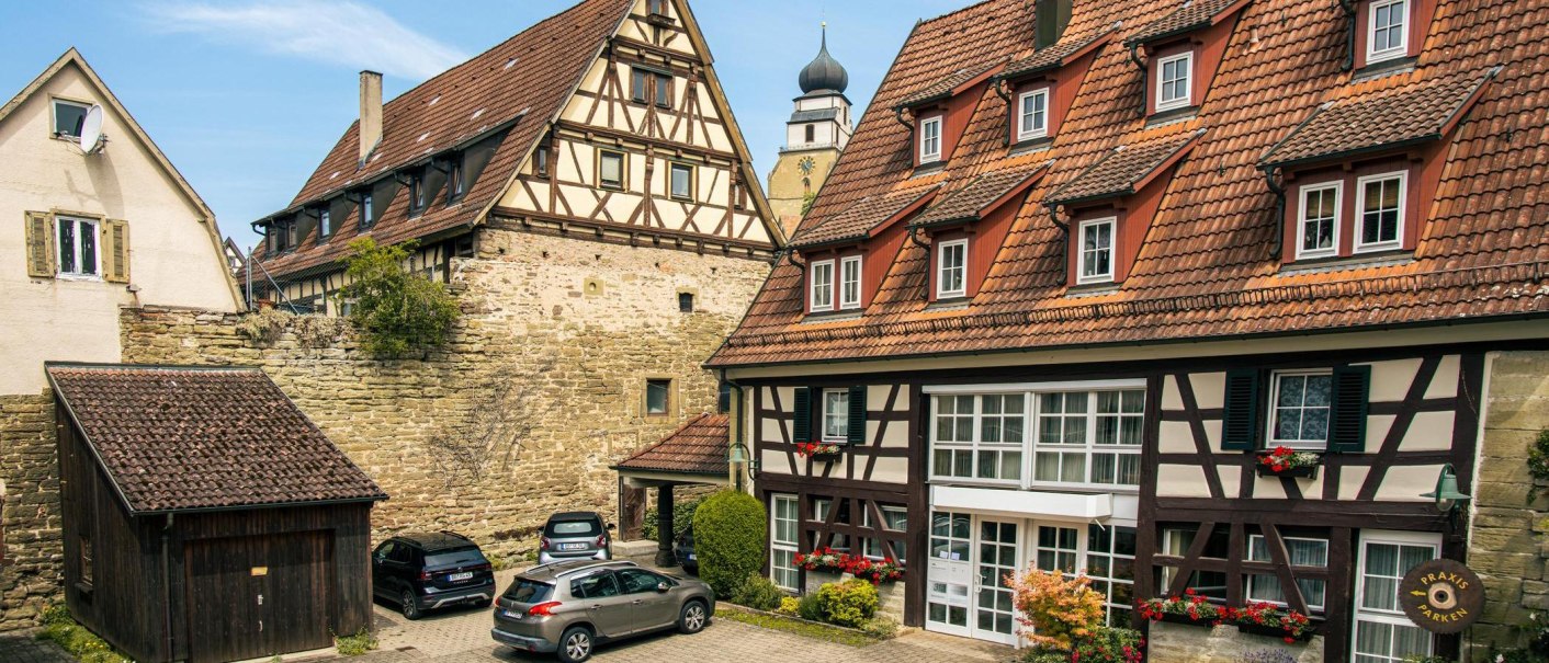 Half-timbered houses in the old town of Herrenberg. Cars are parked in the foreground. A church tower is visible in the background., © Stuttgart-Marketing GmbH, Sarah Schmid