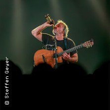 Ein Musiker mit Gitarre trinkt aus einer Flasche auf der Bühne, beleuchtet von Scheinwerfern. Publikum im Vordergrund., © links im Bild Ein Musiker mit Gitarre trinkt aus einer Flasche auf der Bühne, beleuchtet von Scheinwerfern. Publikum im Vordergrund., © links im Bild