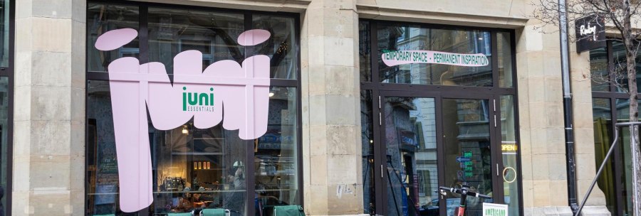 A caf&eacute; with large windows and the words 'juni essentials'. In front of it are bicycles and tables with chairs., &copy; SMG, Sarah Schmid