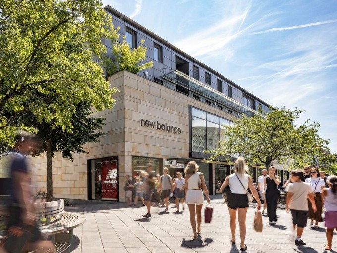 Menschen flanieren an einem New Balance Geschäft in einer sonnigen Einkaufsstraße. Moderne Architektur und Bäume säumen den Weg., © Schlienz-Tours GmbH & Co.KG Menschen flanieren an einem New Balance Geschäft in einer sonnigen Einkaufsstraße. Moderne Architektur und Bäume säumen den Weg., © Schlienz-Tours GmbH & Co.KG