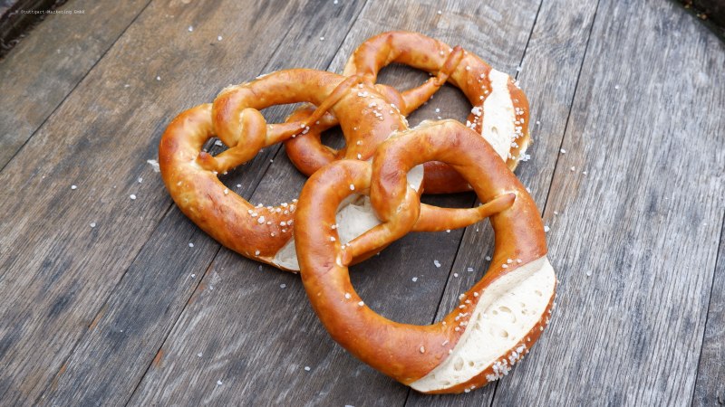 Drei frische Brezeln mit grobem Salz liegen auf einem rustikalen Holztisch., &copy; Stuttgart Marketing GmbH