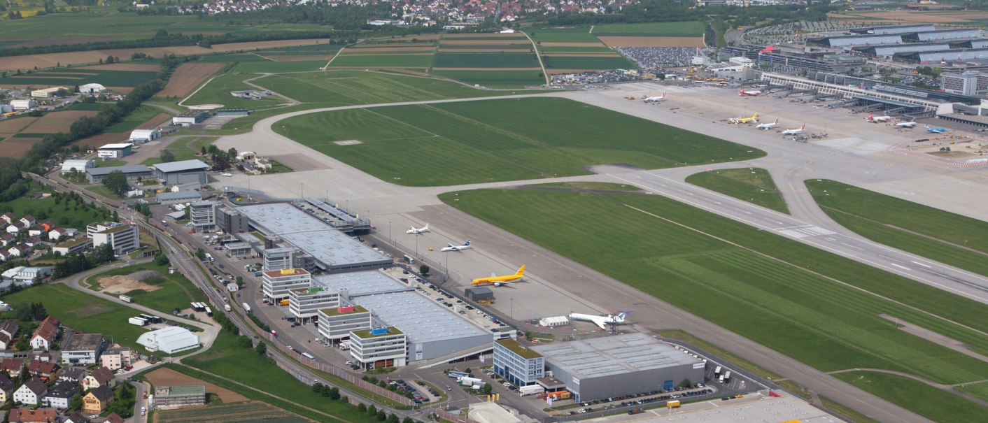 Aerial view of Stuttgart Airport showing runways, parked airplanes, and surrounding buildings. Fields and residential areas can be seen in the background., © © Stuttgart-Marketing GmbH Aerial view of Stuttgart Airport showing runways, parked airplanes, and surrounding buildings. Fields and residential areas can be seen in the background., © © Stuttgart-Marketing GmbH