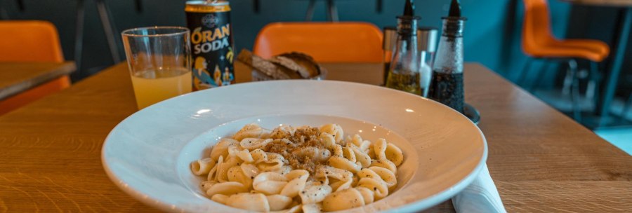 A plate of pasta with sauce, a glass of orange juice and a can of orange soda on a table in a restaurant., &copy; SMG, Sarah Schmid
