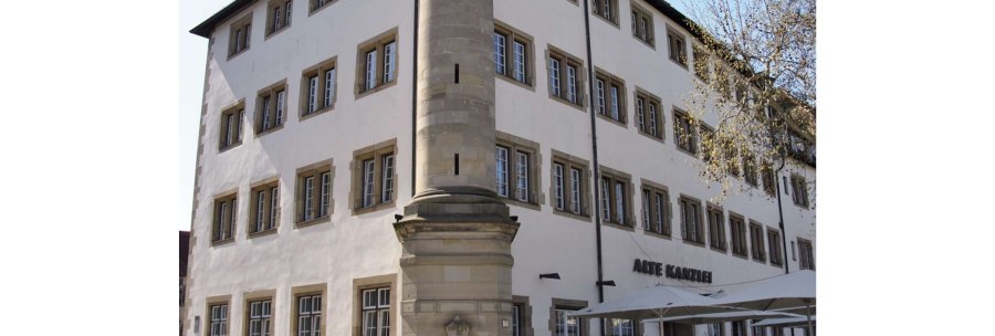 Die Alte Kanzlei in Stuttgart, ein historisches Gebäude mit vielen Fenstern, einem markanten Eckpfeiler und einem Außenbereich mit Sonnenschirmen., © Stuttgart-Marketing GmbH