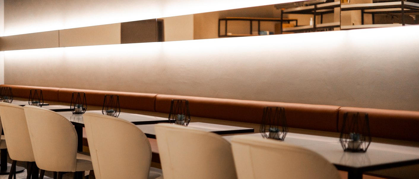 Moderne Restaurant-Inneneinrichtung mit weißen Stühlen und Tischen, beleuchtet durch eine lange Wandlampe., © GINN Apartments Esslingen Moderne Restaurant-Inneneinrichtung mit weißen Stühlen und Tischen, beleuchtet durch eine lange Wandlampe., © GINN Apartments Esslingen