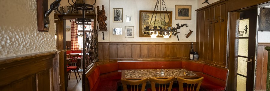 Cozy wine bar with wooden furniture, red upholstery and rustic decoration. Pictures and tools hang on the walls and a chandelier illuminates the room., © SMG Stuttgart Marketing GmbH - Sarah Schmid