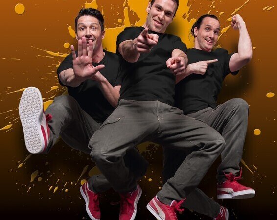Drei Männer in schwarzen T-Shirts und roten Schuhen springen vor einem orangefarbenen Hintergrund mit Farbspritzern., © Theaterhaus Stuttgart e.V. Drei Männer in schwarzen T-Shirts und roten Schuhen springen vor einem orangefarbenen Hintergrund mit Farbspritzern., © Theaterhaus Stuttgart e.V.