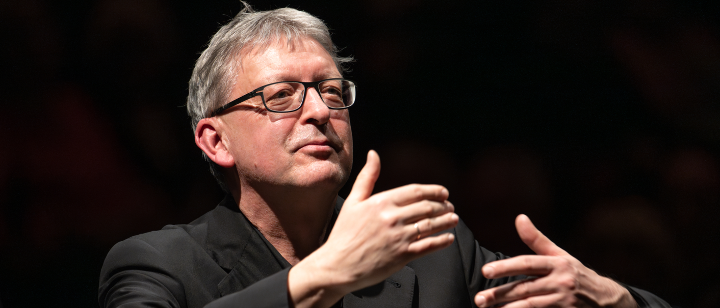 A man with glasses conducts with expressive gestures in front of a dark background., &copy; Holger Schneider