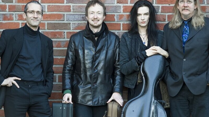 Vier M&auml;nner in schwarzer Kleidung posieren vor einer Ziegelwand. Sie halten Musikinstrumentenkoffer und wirken professionell und stilvoll., &copy; Musik Podium Stuttgart e.V.