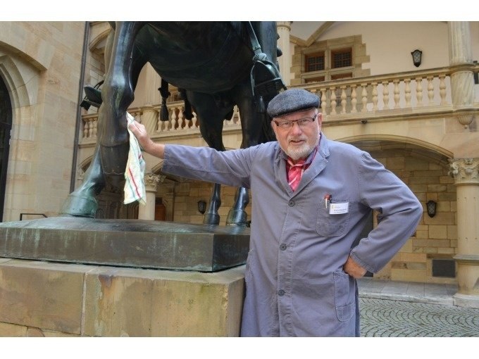 Ein Mann in grauer Arbeitskleidung und Mütze reinigt eine Pferdestatue in einem historischen Innenhof., © Stuttgart Marketing GmbH Ein Mann in grauer Arbeitskleidung und Mütze reinigt eine Pferdestatue in einem historischen Innenhof., © Stuttgart Marketing GmbH