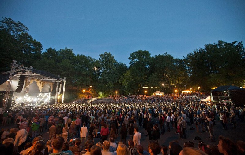 Open-Air-Konzert bei Abenddämmerung, große Menschenmenge vor einer beleuchteten Bühne, umgeben von Bäumen., © Württembergische Staatstheater Stuttgart Open-Air-Konzert bei Abenddämmerung, große Menschenmenge vor einer beleuchteten Bühne, umgeben von Bäumen., © Württembergische Staatstheater Stuttgart